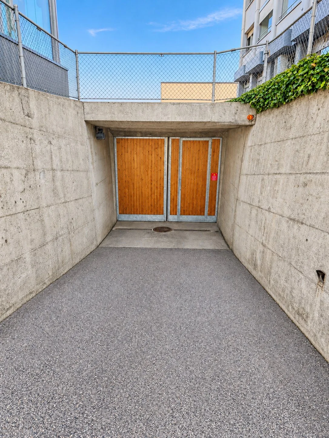 Die Einfahrt zur Tiefgarage an der Aarauerstrasse 8 in Reinach AG: Rampe zwischen Betonwänden mit einem zweiflügligen Holztor.